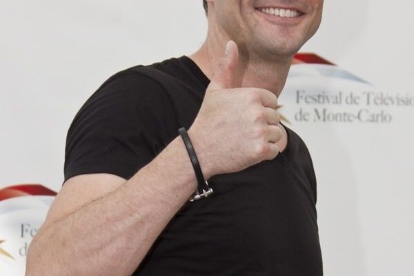 A man in a black t-shirt giving a thumbs-up gesture.