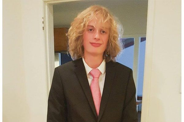 A blonde young man wearing a black suit and pink tie