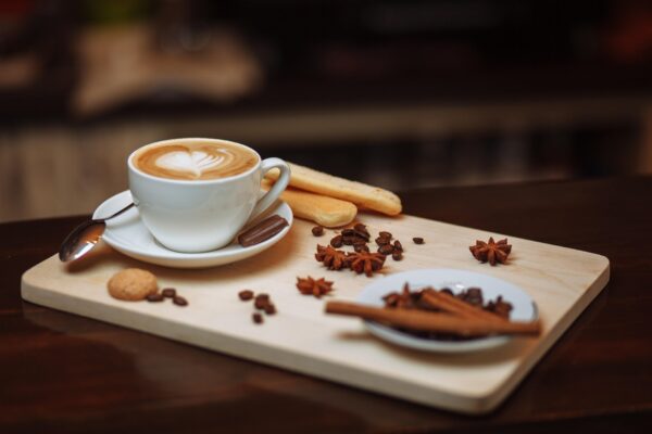 A cup of coffee with cookies and cinnamon sticks on a wooden tray.