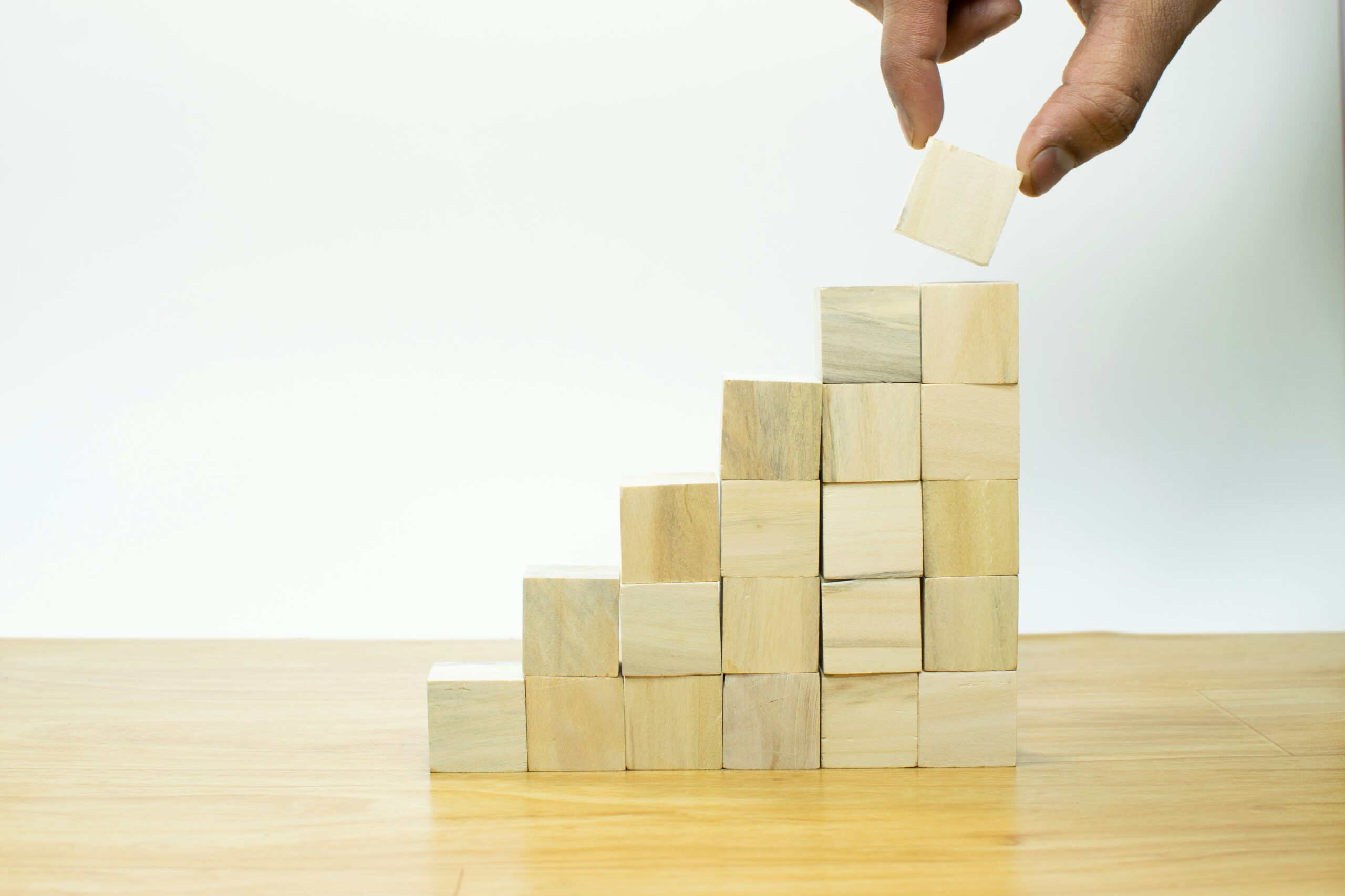 A hand placing the final wooden block on top of a staircase-shaped stack.