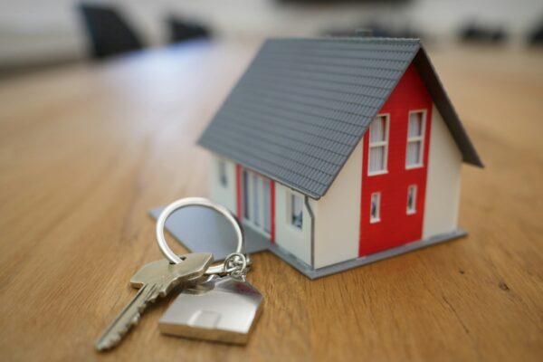 A small model house with a set of silver keys on a wooden table.