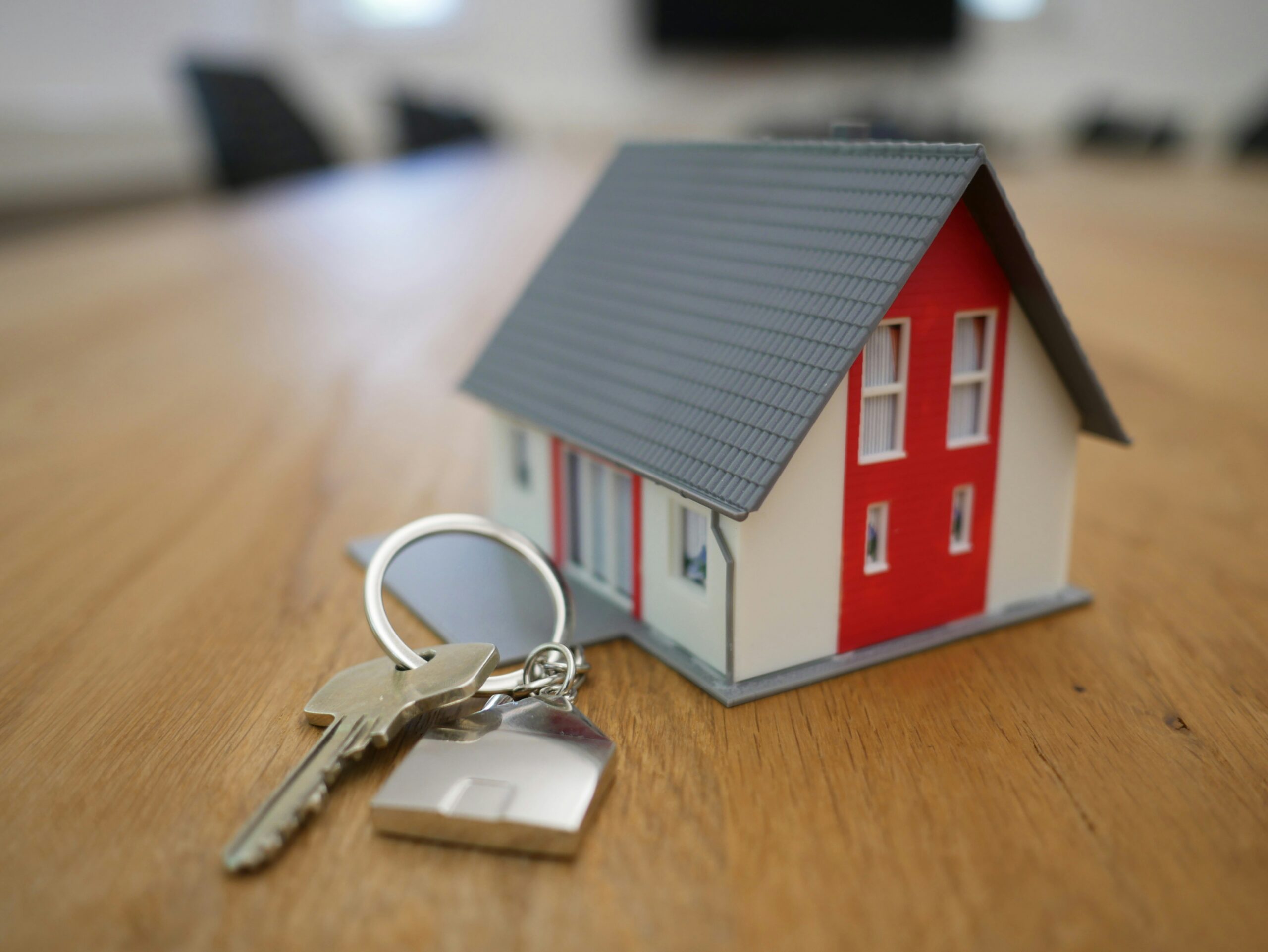 A small model house with a set of silver keys on a wooden table.