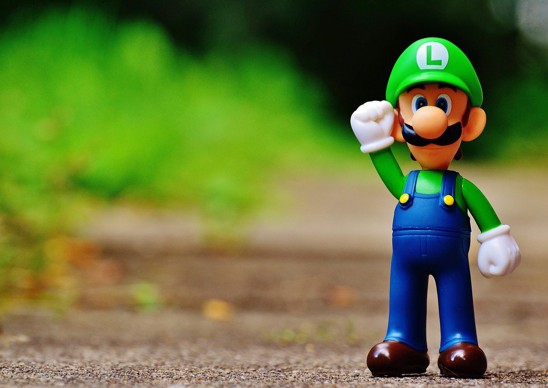A small Luigi toy figure standing on a wooden surface against a blurry green background.