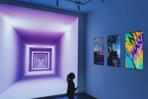 A person standing in a modern art gallery looking at glowing purple wall art.