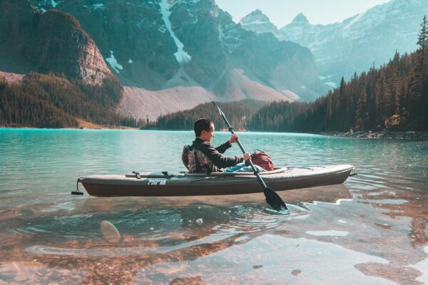A person paddling a kayak on a calm lake surrounded by mountains.