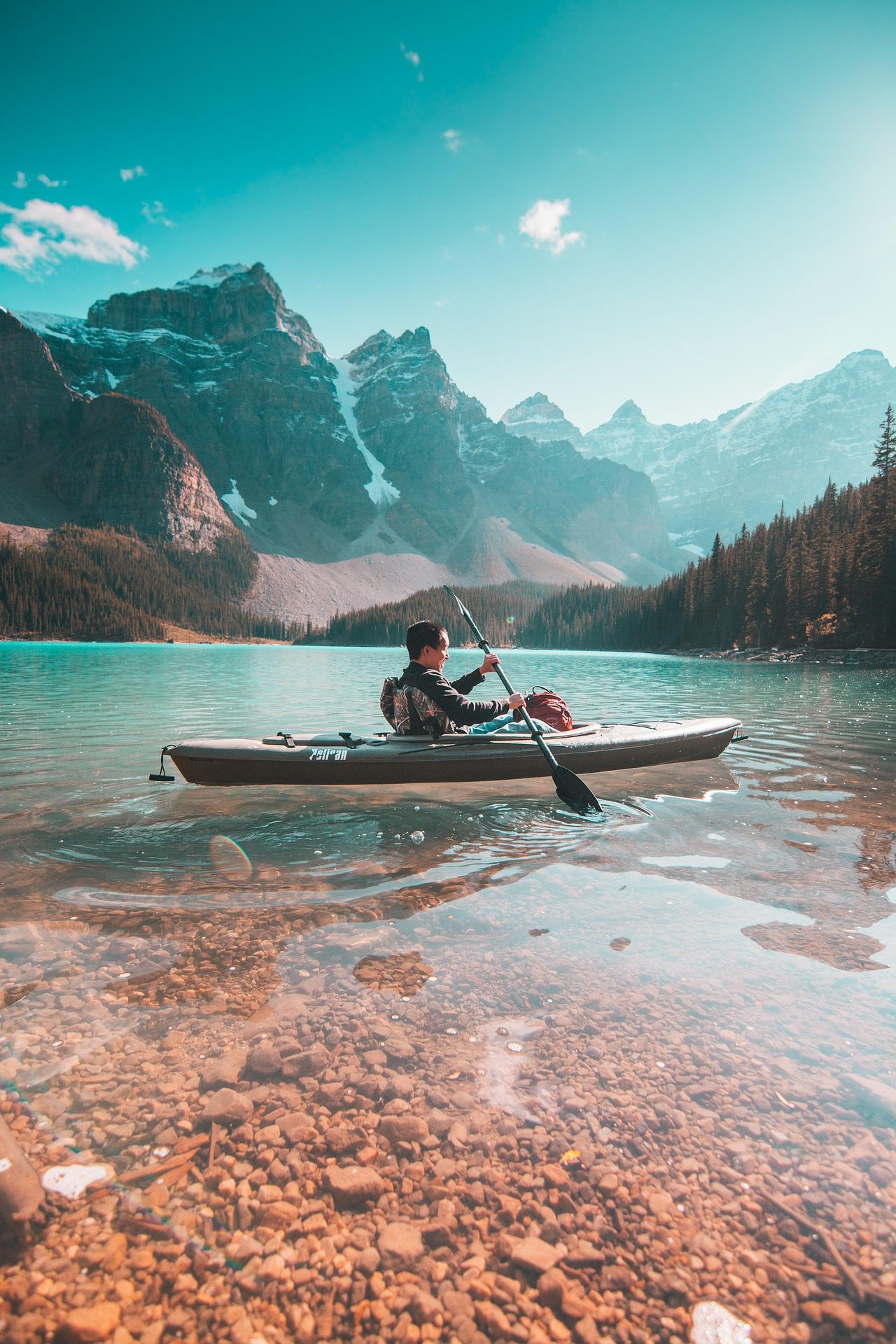 A person paddling a kayak on a calm lake surrounded by mountains.