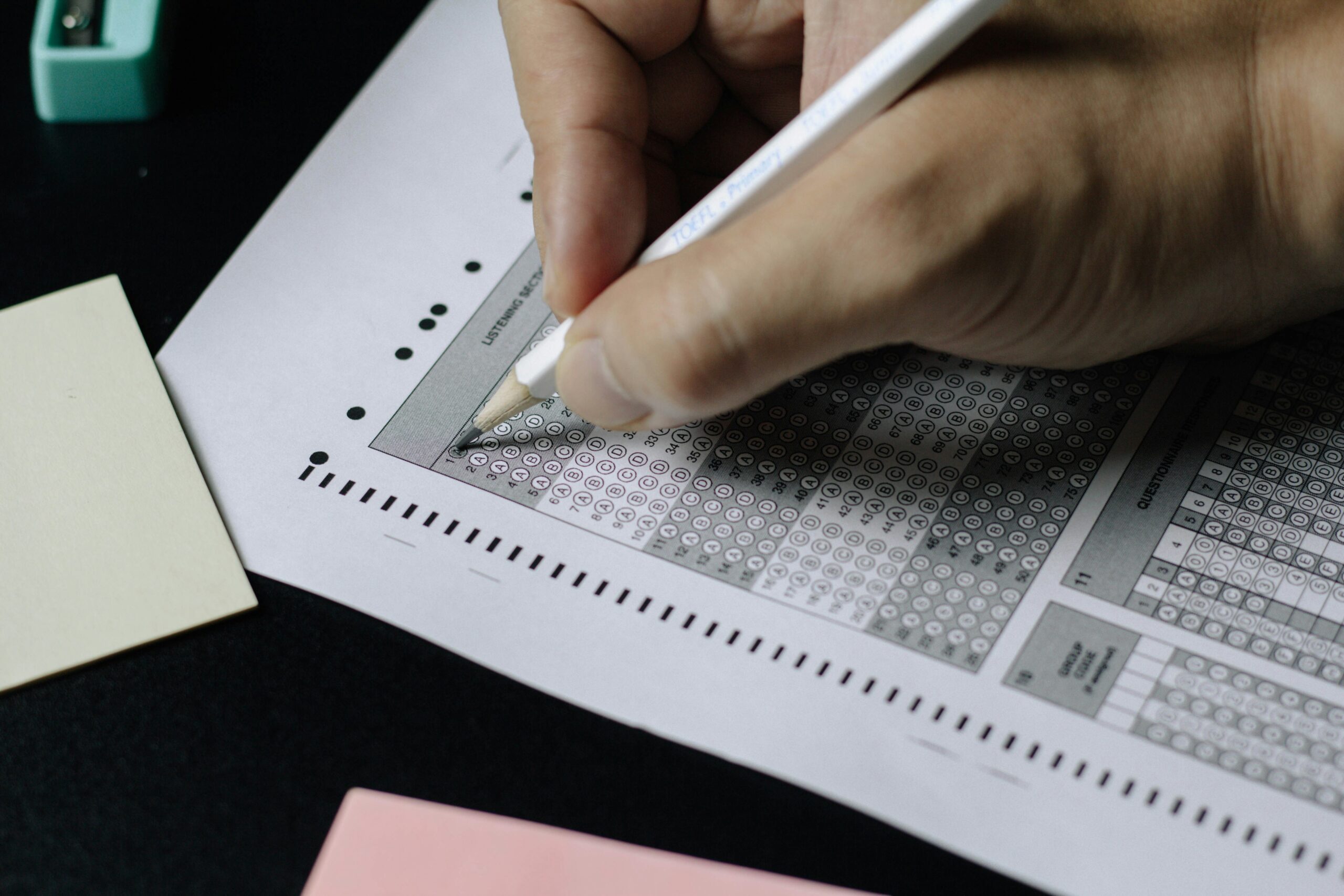 A person filling out an OMR sheet (multiple-choice answer sheet) with a pen.