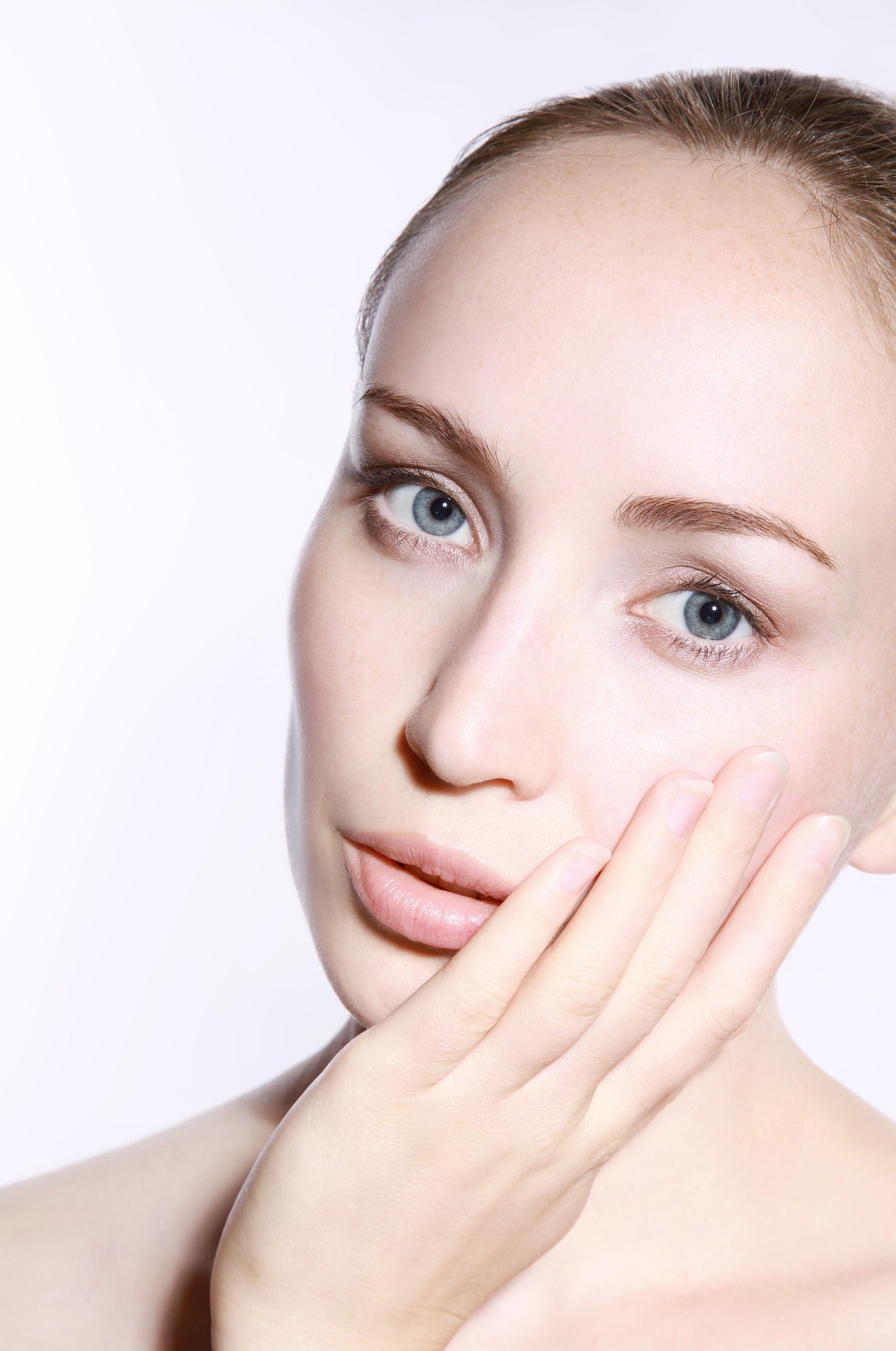 A close-up of a woman’s face with her hand touching her cheek, representing beauty or skincare.