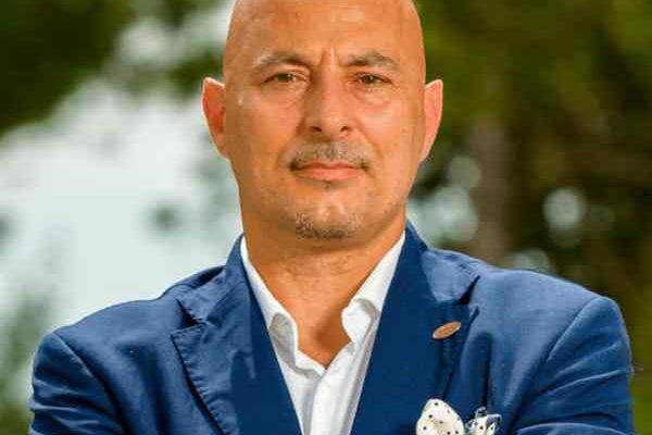 A bald man in a blue blazer smiling outdoors.