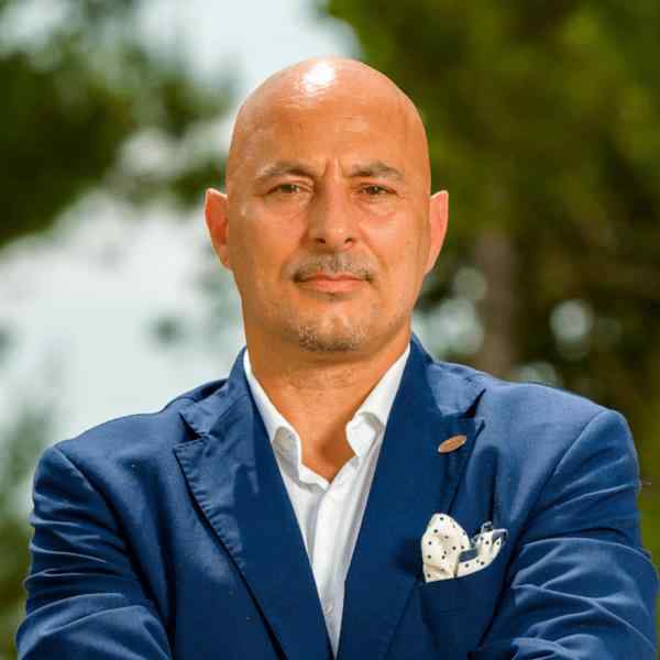 A bald man in a blue blazer smiling outdoors.
