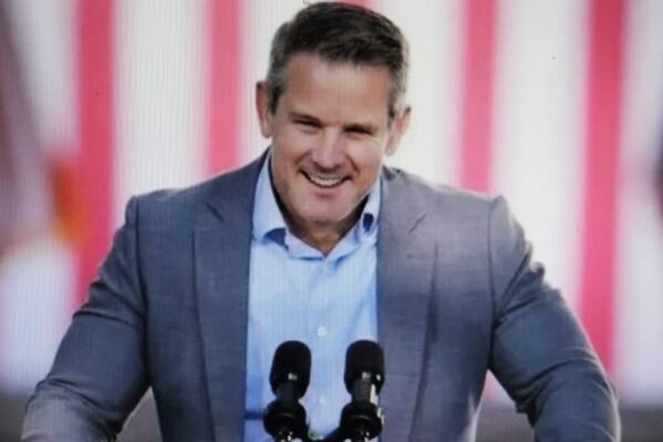 A man in a grey suit speaking at a podium with microphones.