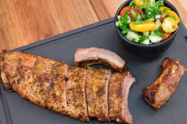 Sliced grilled ribs served on a black tray with a side of salad.