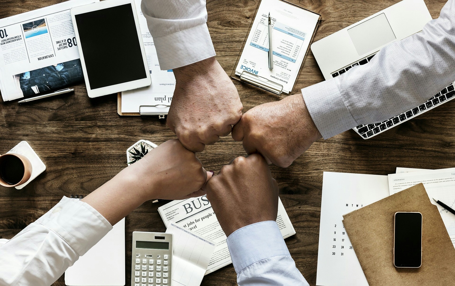 Four people putting their fists together over a desk.