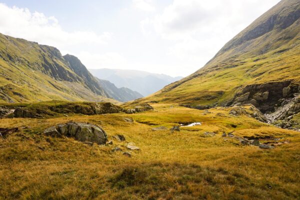 A scenic landscape of a lush green mountain valley under a bright sky.
